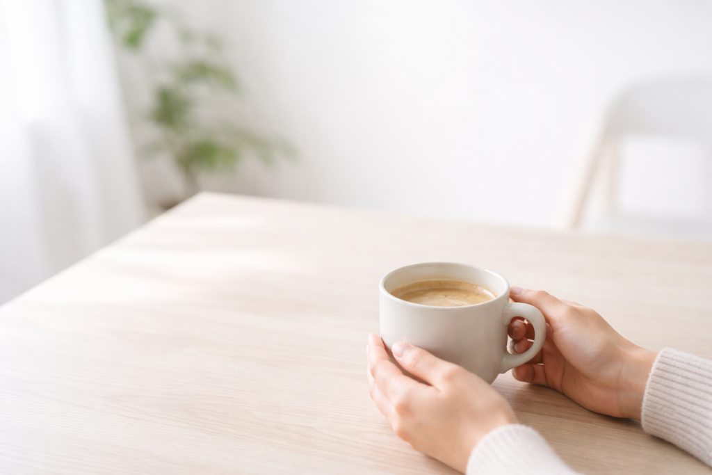 Baggrund til call-to-action sektion: lys og luftig scene med hænder, der rækker ud efter en kop kaffe på et rent bord, med masser af negativ plads til tekst.